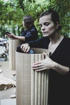 a woman holding a bottle in her hand next to a cardboard container with wood sticks sticking out of it