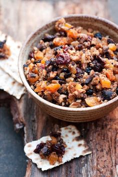 a bowl filled with food sitting on top of a wooden table next to crackers