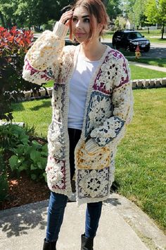 a woman is standing on the sidewalk with her hand in her hair and wearing a crocheted cardigan