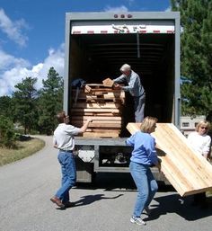 three people unloading wood from the back of a truck