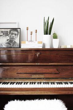 an old piano is sitting in front of a shelf with plants and pictures on it