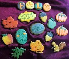 decorated cookies are arranged in the shape of autumn leaves and acorns on a purple cloth