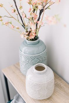 a white vase with flowers in it sitting on a table next to a blue vase