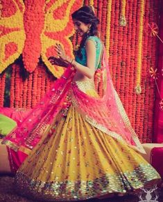 a woman in a yellow and pink lehenga standing next to orange flower wall