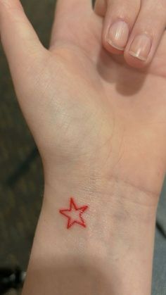 a small red star tattoo on the left wrist and right hand, with an arrow in the middle