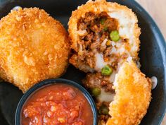 some fried food on a black plate with sauce and ketchup in a bowl