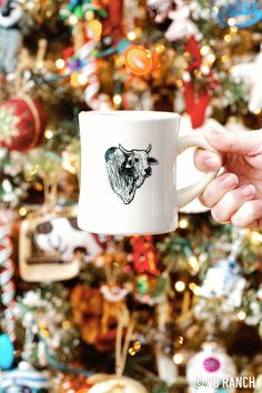 a person holding a coffee mug in front of a christmas tree with ornaments on it