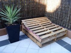 a bed made out of wooden pallets next to a potted plant