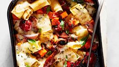 a casserole dish filled with pasta, vegetables and meats on a white surface