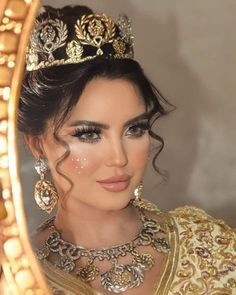 a woman wearing a tiara in front of a mirror with gold jewelry on it