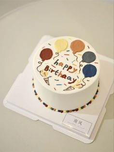 a white birthday cake with balloons and confetti on the top is sitting on a plate