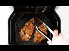 two pieces of chicken being cooked in an air fryer with tongs on the side