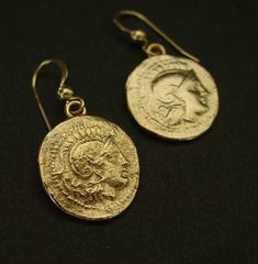 two gold coin earrings on a black surface, one has a head and the other has a face