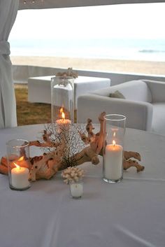 two candles are sitting on a table next to some glass vases and driftwood