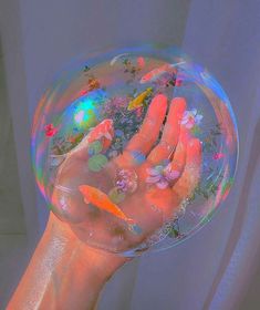 a person's hand holding a soap bubble filled with water and colorful fish in it