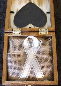 an open wooden box with some silver ribbon and a black piece of cloth in it