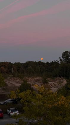 the sun is setting over some trees and cars