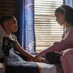 a woman sitting next to a boy on top of a bed in front of a window