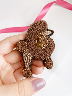 a hand holding a brown brooch with beading on it and a pink ribbon