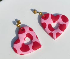 two red and pink heart shaped earrings on a white surface with gold earring hooks