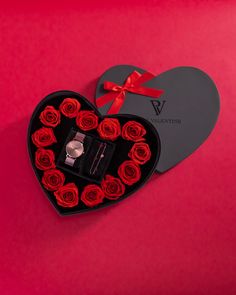 a heart shaped box with red roses in it and a ring on the inside, sitting next to a watch