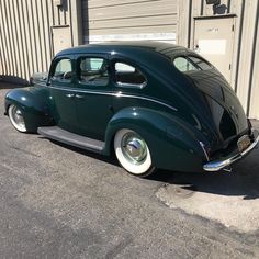 an old green car is parked in front of a building with garage doors on the side