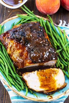 a plate with meat and green beans on it next to some peaches, an apple