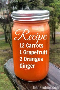 a jar filled with carrots sitting on top of a wooden table next to trees