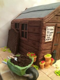 there is a cake made to look like a log cabin and wheelbarrow with dirt in it