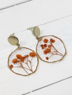 a pair of earrings with dried flowers in them on a white wooden background, close up