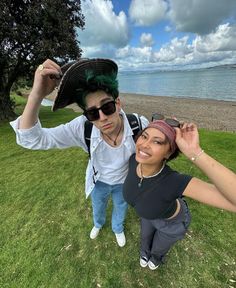 a man and woman posing for a photo in front of the ocean with green hair