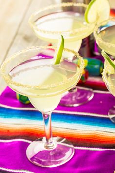 three margaritas sitting on top of a colorful table cloth