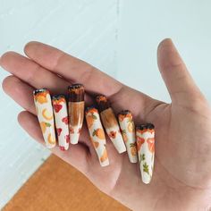 four different sized nails with flowers on them in someone's hand, one is orange and the other is white