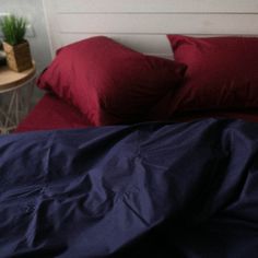 an unmade bed with red sheets and pillows on top of it, next to a small table