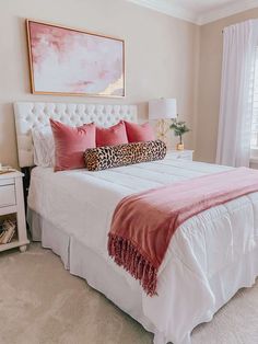 a white bed topped with pink pillows and a leopard print throw pillow on top of it