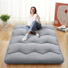 a woman sitting on top of a mattress in the middle of a wooden floor next to a potted plant