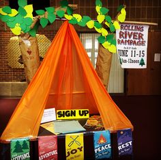 a tent made out of orange plastic bags with trees on it and signs in the background