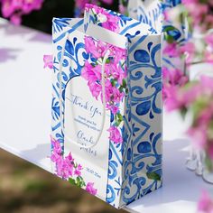 a blue and white bag sitting on top of a table next to pink flowers in vases