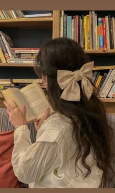 a woman sitting on a couch reading a book with a big bow in her hair