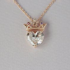 a heart shaped necklace with a crown on the front and two small diamonds in the middle