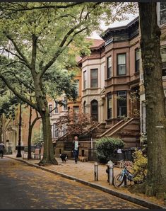 people are walking down the sidewalk in front of some buildings and trees on a sunny day