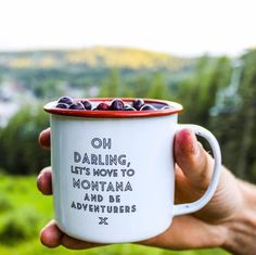 a person holding a coffee mug with blueberries in it that says oh daring, lets move to montana and be adventurers x