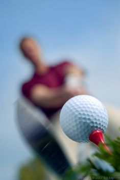 a golf ball sitting on top of a tee next to a man in red shirt