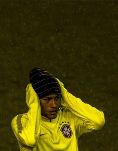 a soccer player is holding his head with one hand and wearing a yellow shirt while standing in the rain