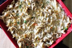 a red casserole dish filled with pasta and vegetables on top of a wooden table