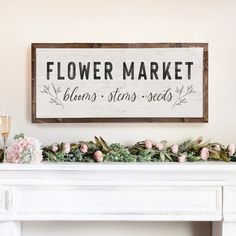 a sign that says flower market hangs above a mantel with flowers and candles on it