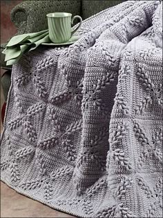 a blanket that is sitting on top of a couch next to a cup and saucer