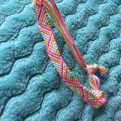 a close up of a piece of fabric on top of a blue blanket with pink and yellow braiding