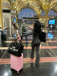 a woman is pulling a pink suitcase through an airport terminal with other people in the background