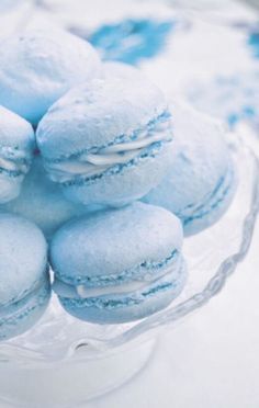 a glass bowl filled with blue macaroons on top of a table